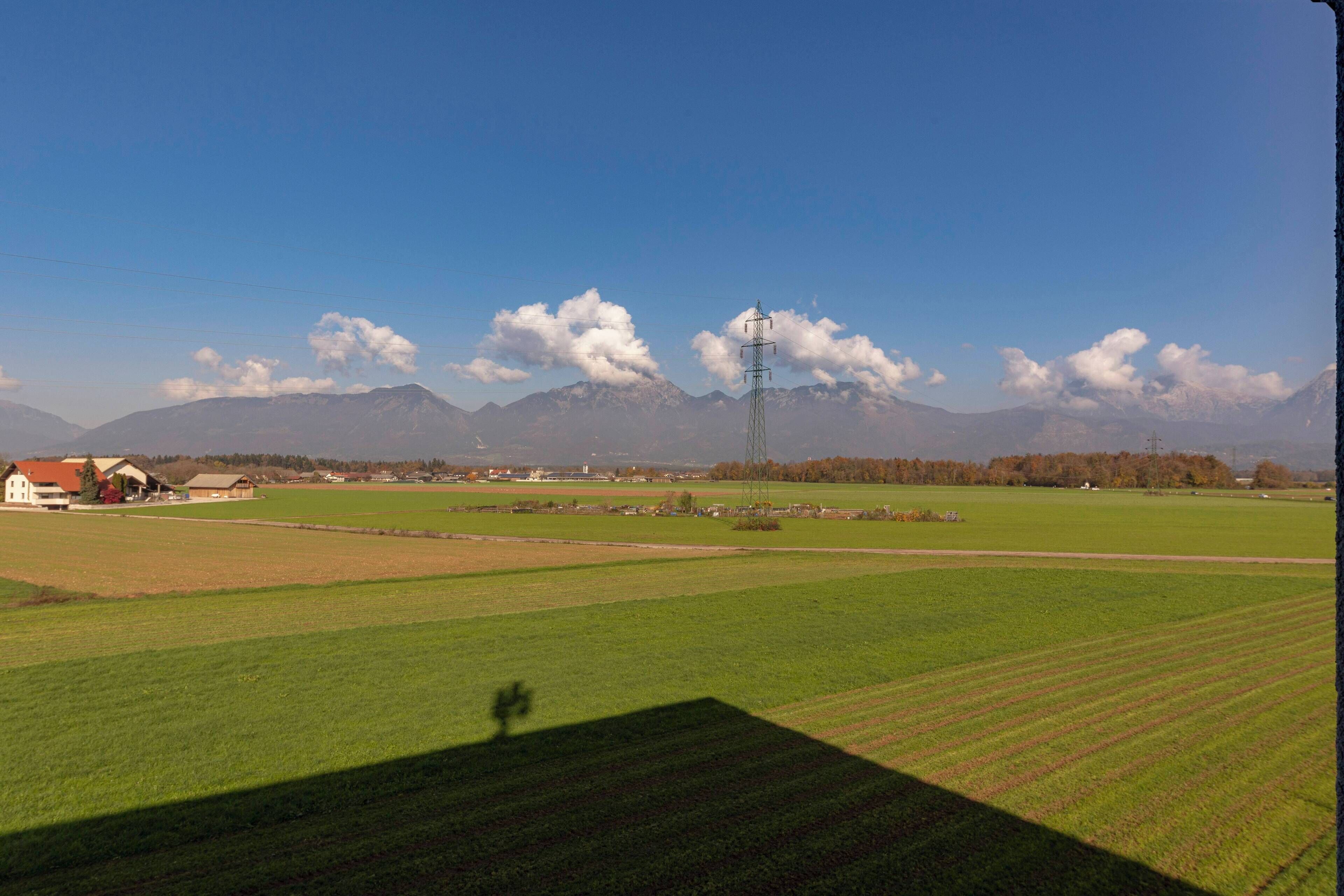 A rural landscape with a clear sky, green fields, and distant mountains.