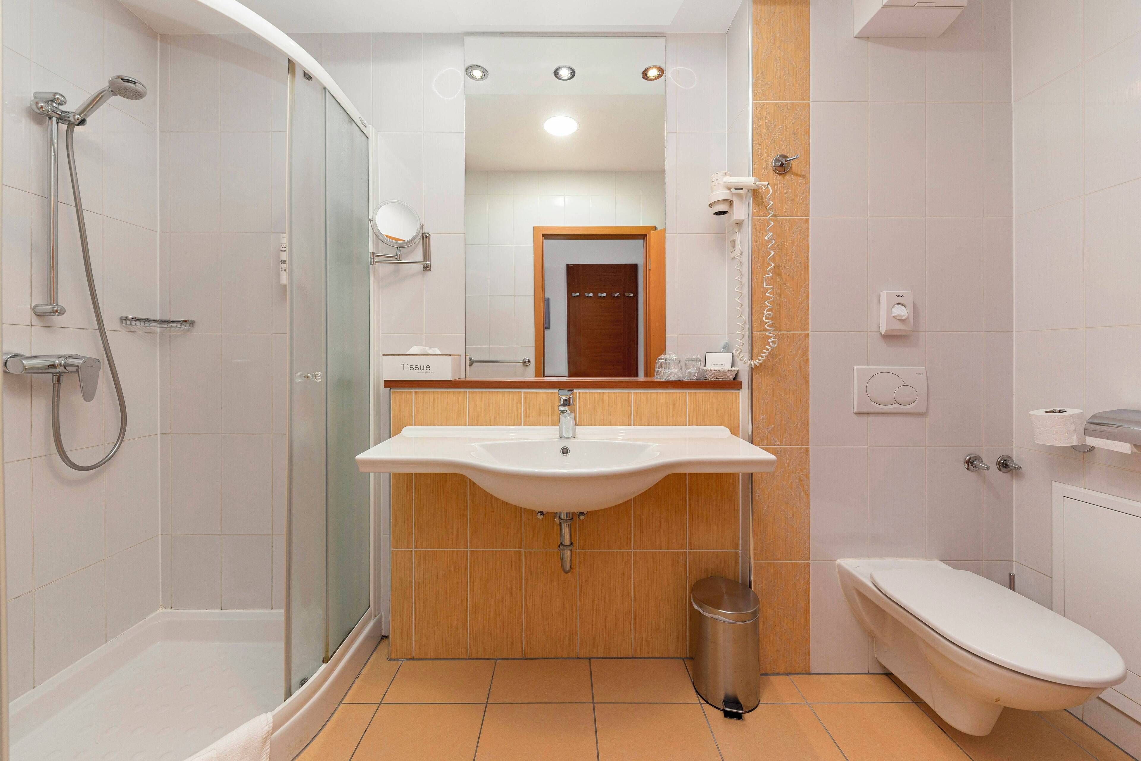 A modern bathroom with a glass-enclosed shower, a white sink, a toilet, and a wooden vanity.