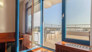 Una habitación con un amplio ventanal corredera que da a una terraza exterior con vistas al horizonte de la ciudad.
