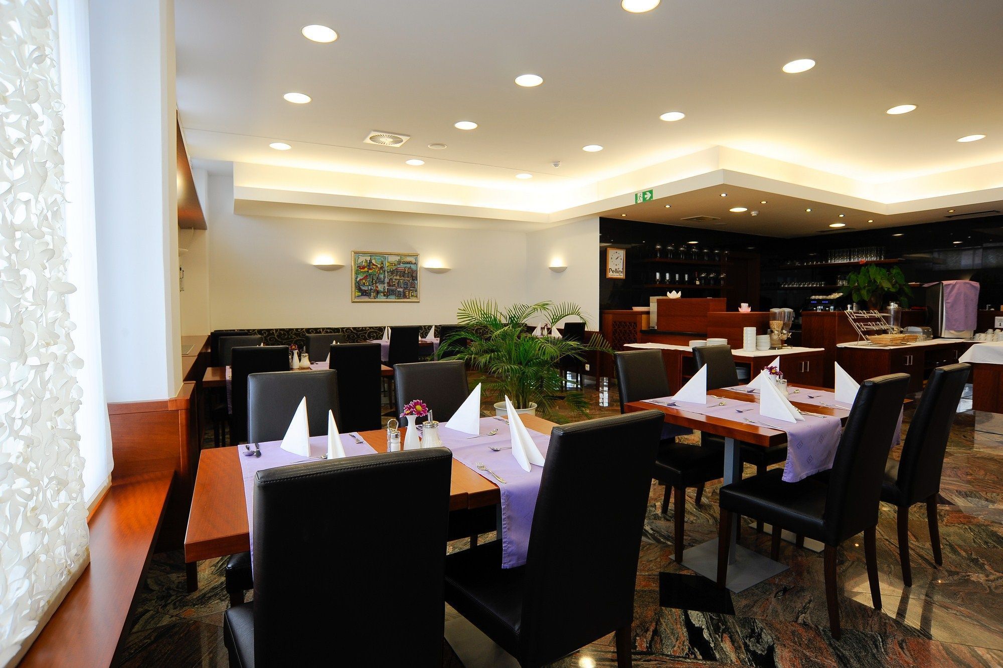 Un restaurant avec des tables dressées pour le service, des chaises et un bar situé au fond de la salle.