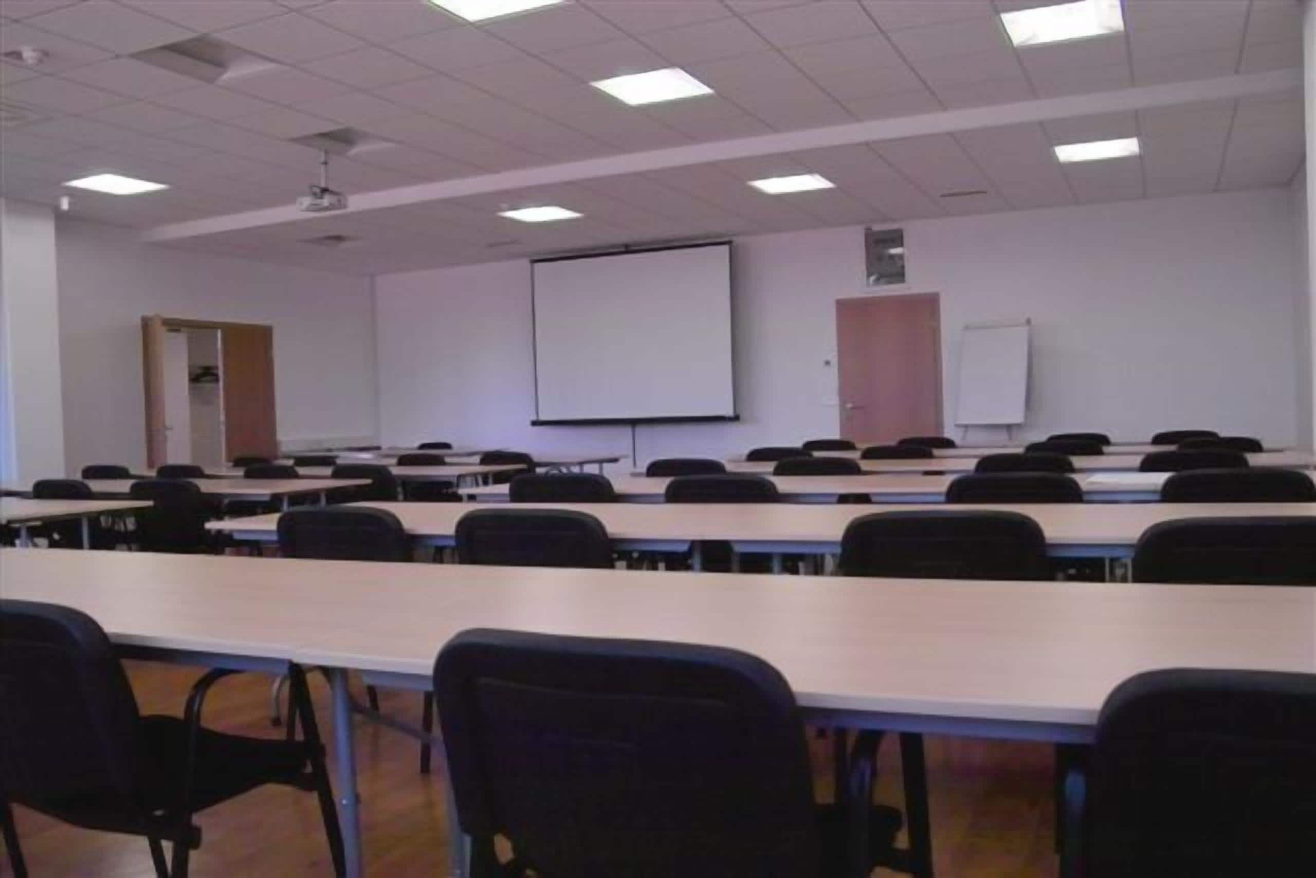 A classroom with rows of desks and chairs, a projector screen, and a whiteboard.