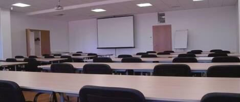 Un aula con filas de escritorios y sillas, una pantalla de proyector y una pizarra.