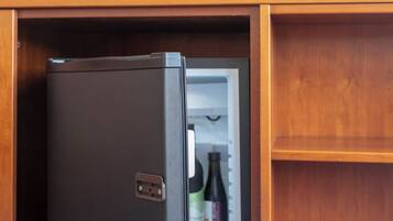 A compact refrigerator in a hotel room with a television mounted on the wall above it.