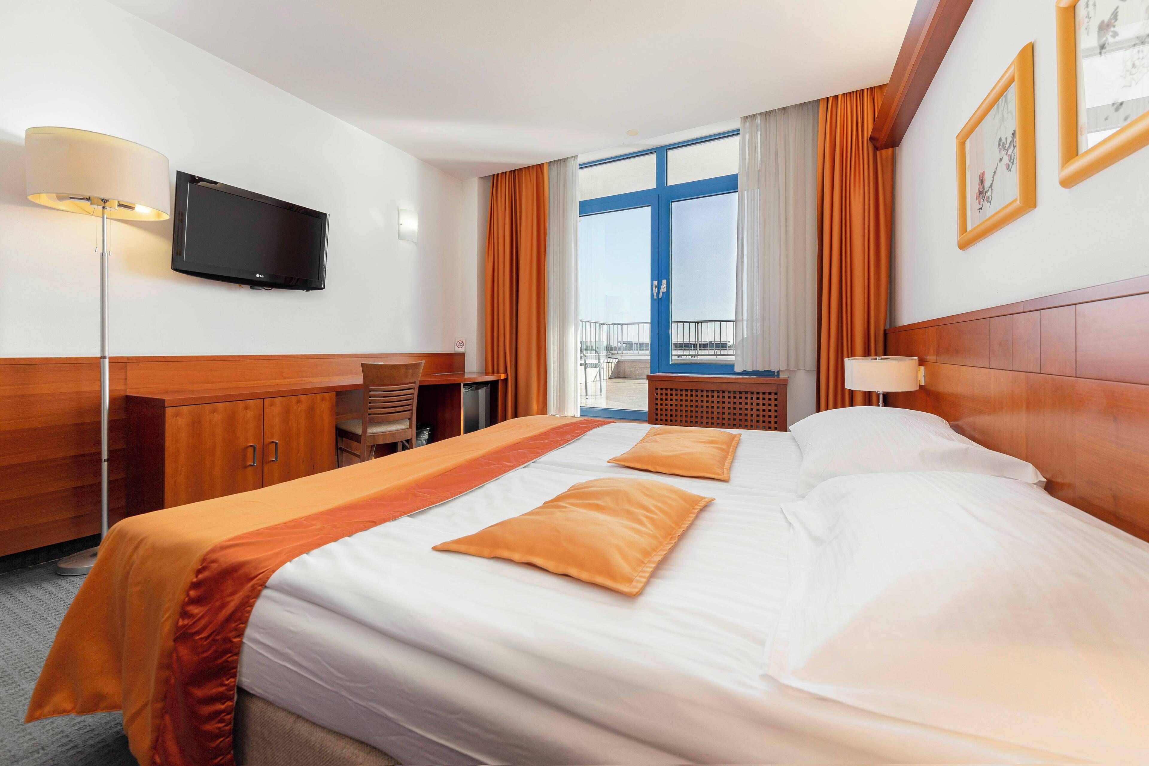 Una camera d'albergo con un letto grande, una scrivania, una televisione e un balcone con vista.