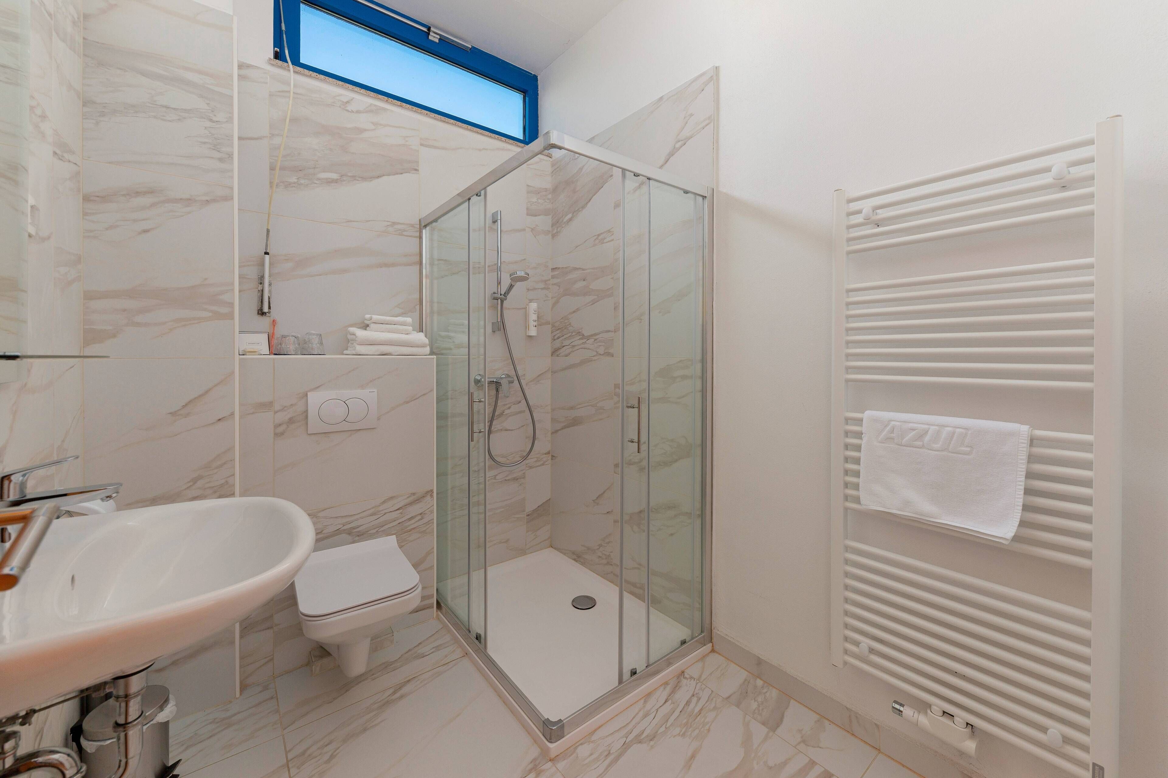 A modern bathroom with a glass-enclosed shower, a white sink, and a toilet.