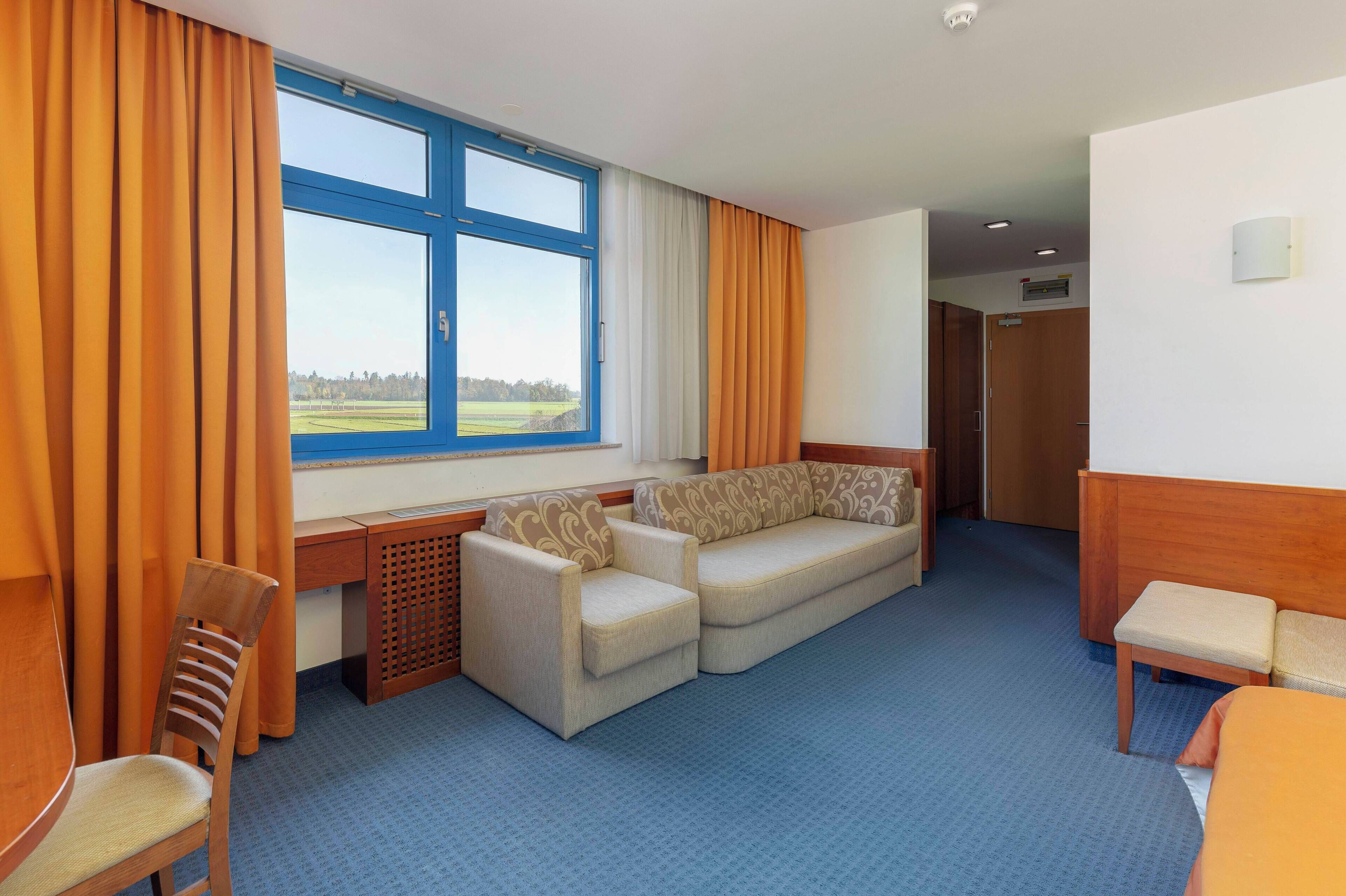 Habitación de hotel con un ventanal grande, un sofá, un escritorio y una silla.