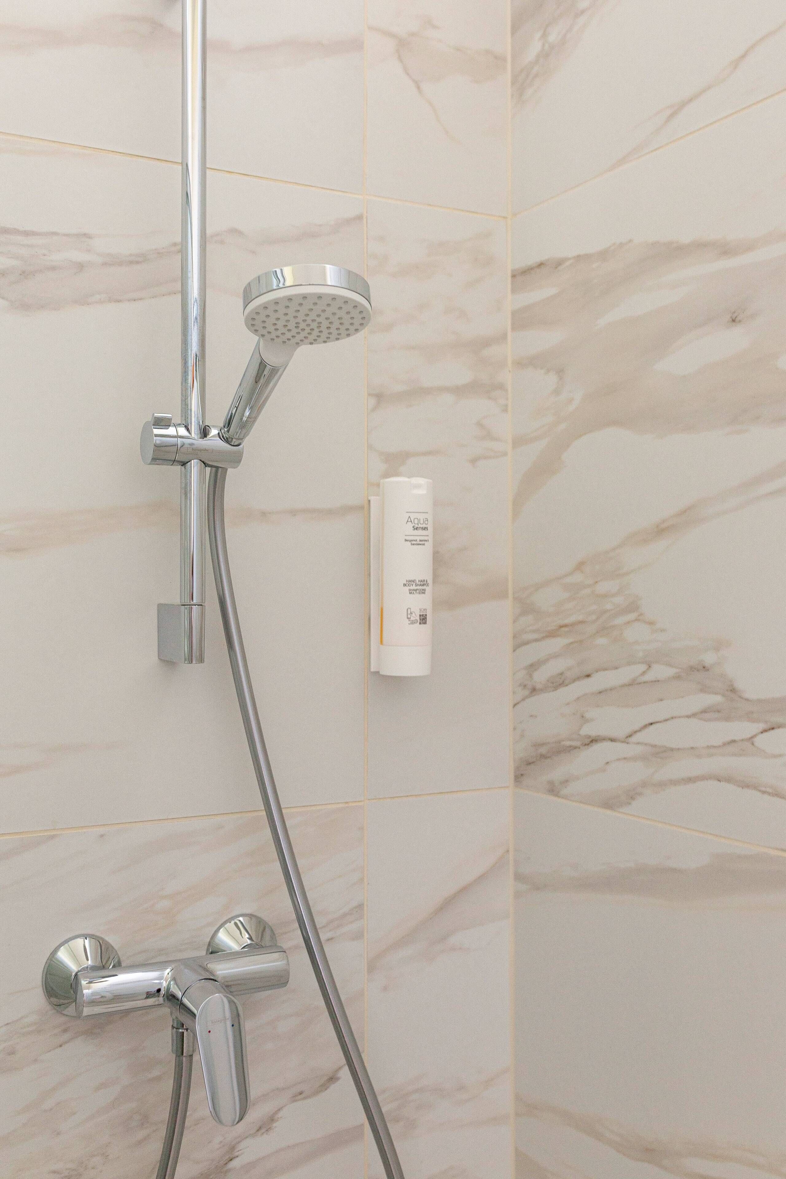 Een badkamer met een douche, douchekop en bedieningspaneel aan de muur.