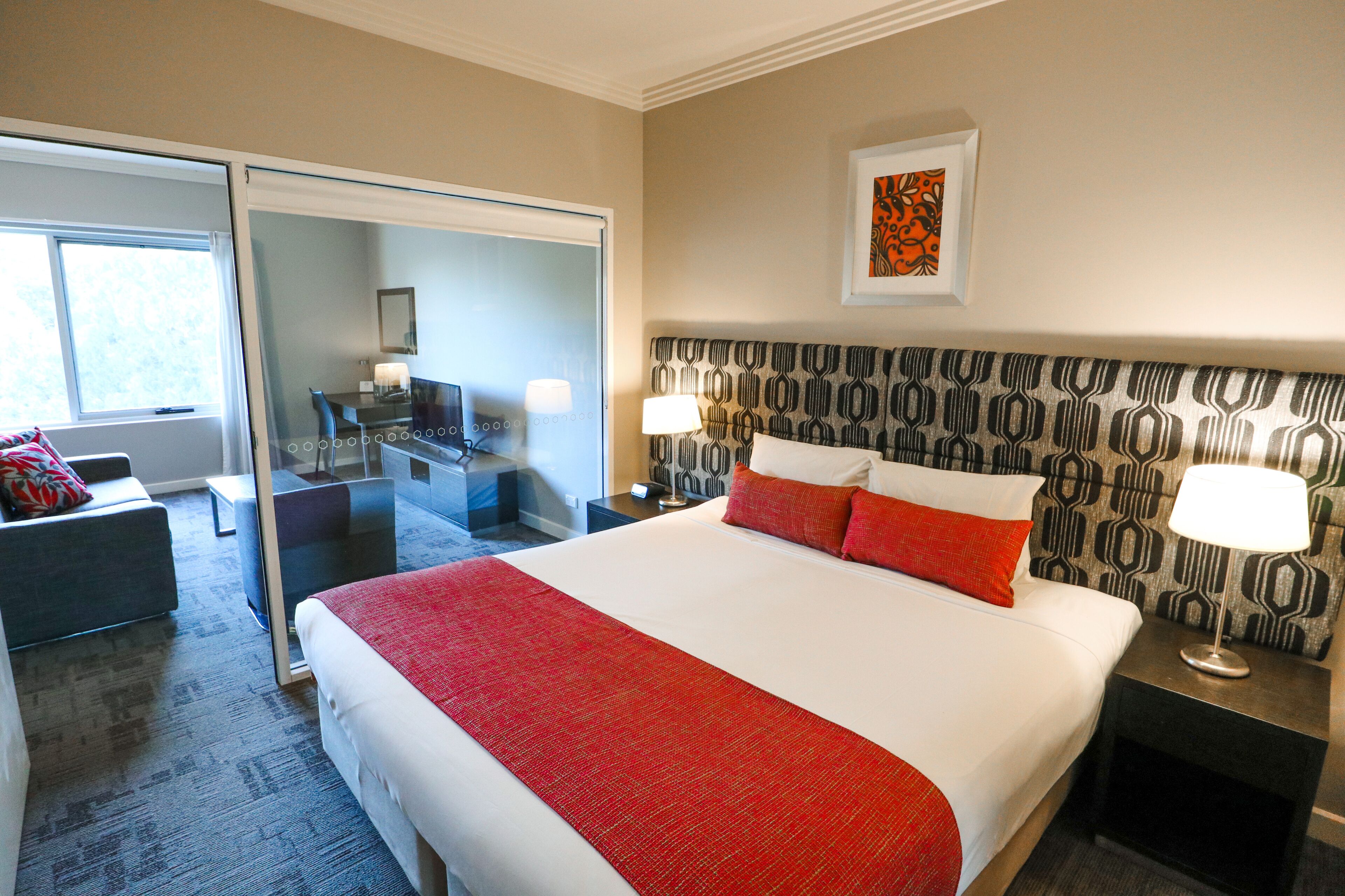 A hotel room with a large bed, a desk, a chair, and a sliding door leading to a balcony.