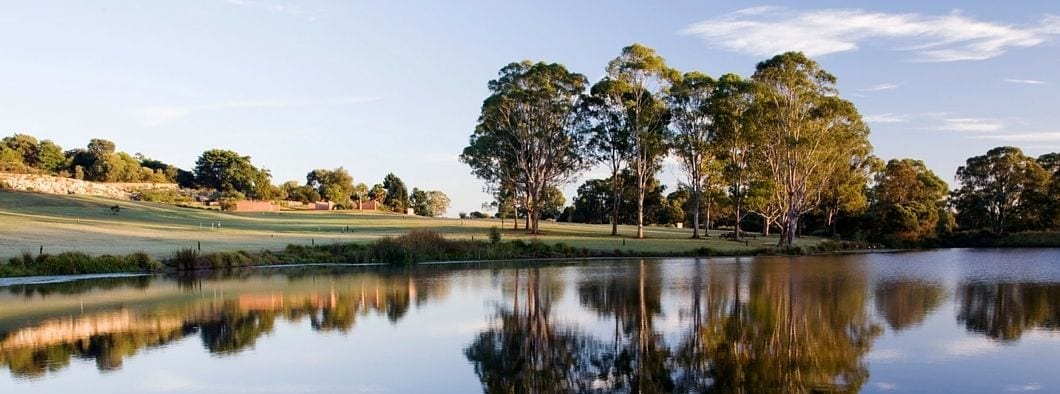 A serene landscape with a calm lake reflecting trees and a golf course.