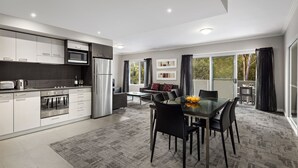 A modern kitchen with stainless steel appliances, a dining area with a glass table, and a view of the outdoors. - Quest Campbelltown (Campbelltown)