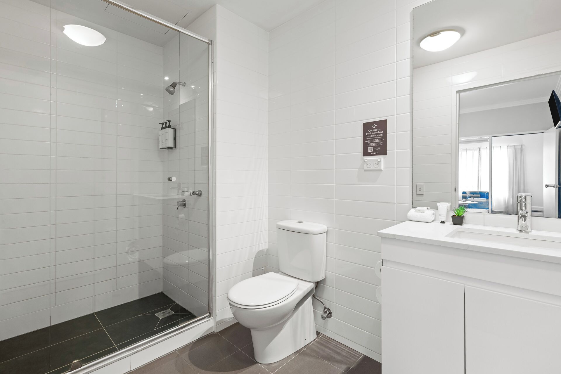 Een moderne badkamer met een douchecabine van glas, een wit toilet en een wastafel met spiegel.