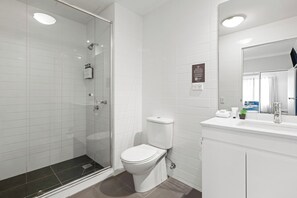 Ein modernes Badezimmer mit einer Glaskabine zur Dusche, einer weißen Toilette und einem Waschtisch mit Spiegel.