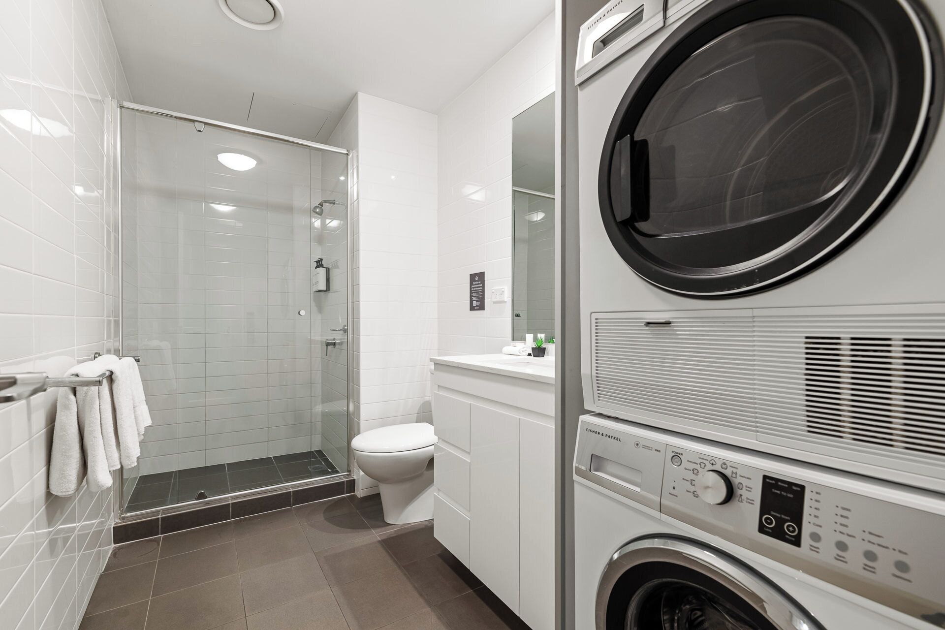 Un baño moderno con cabina de ducha de vidrio, inodoro y lavadora y secadora apiladas.