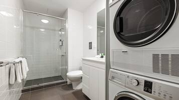 Un baño moderno con cabina de ducha de vidrio, inodoro y lavadora y secadora apiladas.
