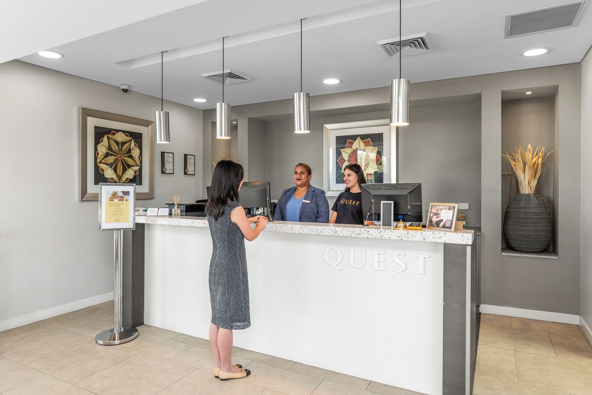 A reception desk with a modern design, featuring a logo, framed artwork, and a vase with decorative reeds.
