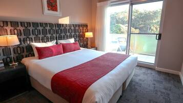 A hotel room with a large bed, two bedside tables with lamps, a patterned headboard, and a view of the outdoors through a sliding glass door.