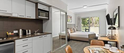 Een moderne hotelkamer met een kitchenette, een bed met uitzicht, een zithoek en een groot raam.