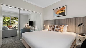 A hotel room with a large bed, a desk with a computer, a TV, and a seating area with a sofa and chairs. - Quest Campbelltown (Campbelltown)