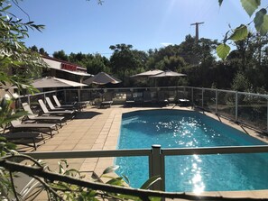 Una piscina con tumbonas y sombrillas, rodeada por una valla y árboles.
