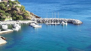 A marina with boats docked, a rocky breakwater, and a hillside with buildings.