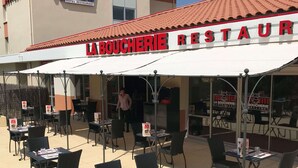 An outdoor seating area of La Boucherie Restaurant with tables and chairs arranged under a white awning.