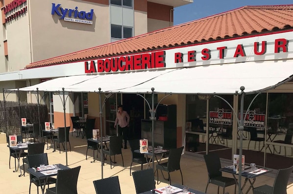 Un área de estar al aire libre del restaurante La Boucherie, con mesas y sillas dispuestas bajo un toldo blanco.