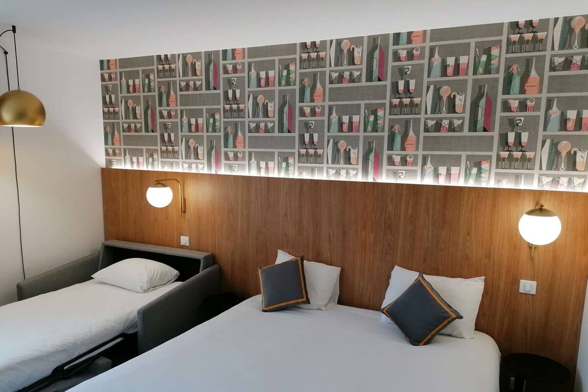 A hotel room with two single beds, a wooden headboard, and a wall decorated with a pattern of various bottles and glasses.