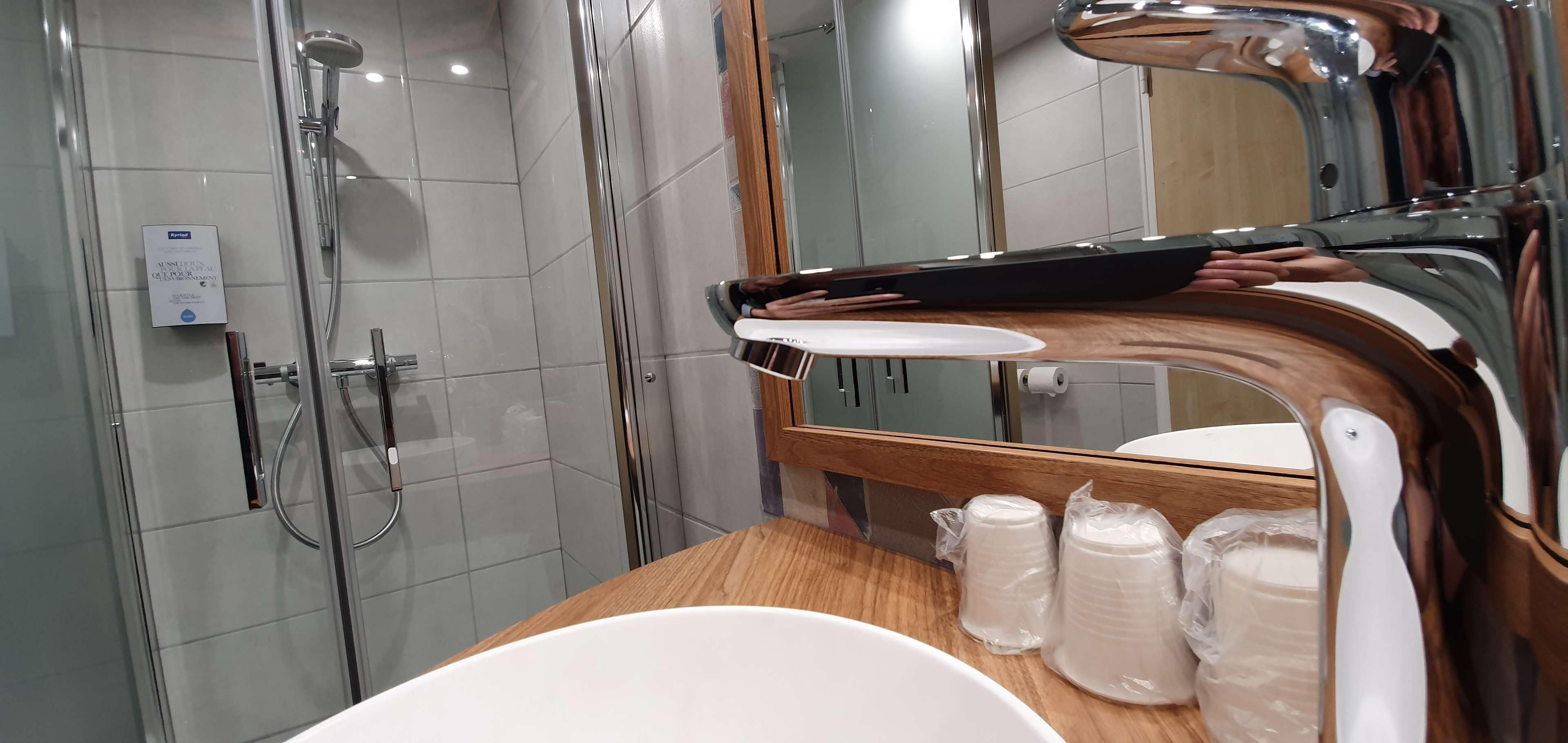 Une salle de bain moderne avec une douche à parois de verre, un meuble-lavabo en bois et un grand miroir.