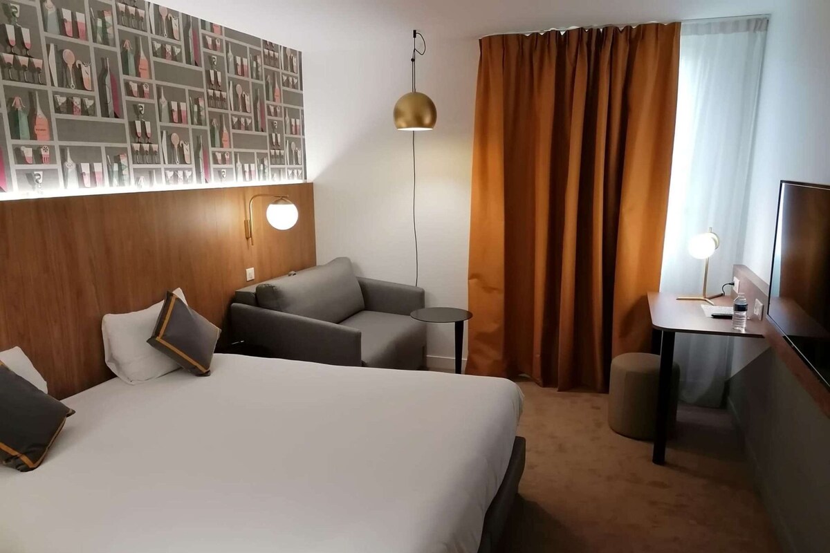 A hotel room with a large bed, a sofa, a desk, and a wall-mounted artwork.
