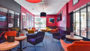 A modern interior with vibrant orange and purple chairs, a wooden table, and a large red pendant light.