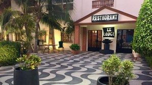 Entrada de hotel con un letrero que dice 'RESTAURANT' y un letrero que dice 'LE LODGE', rodeada de plantas en macetas y un camino con diseño.