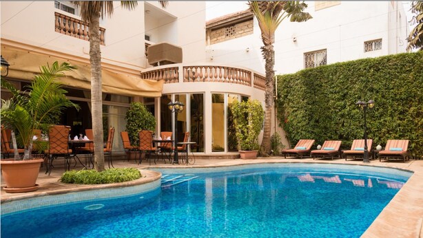Zona de piscina con sillones de descanso, un espacio de estar cubierto y una pared de vegetación.