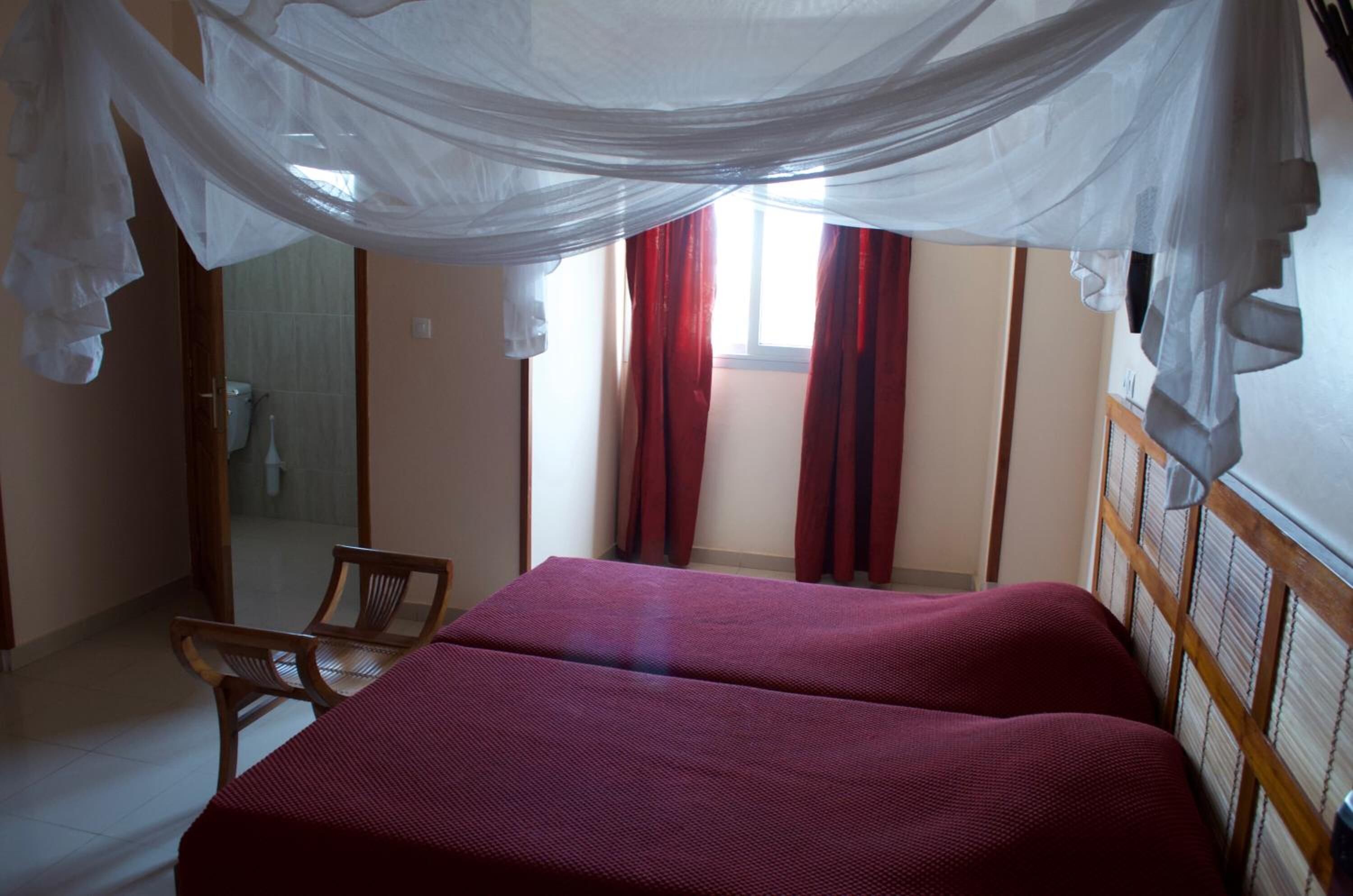 Una habitació amb dos llits, una cadira i una finestra amb cortines.
