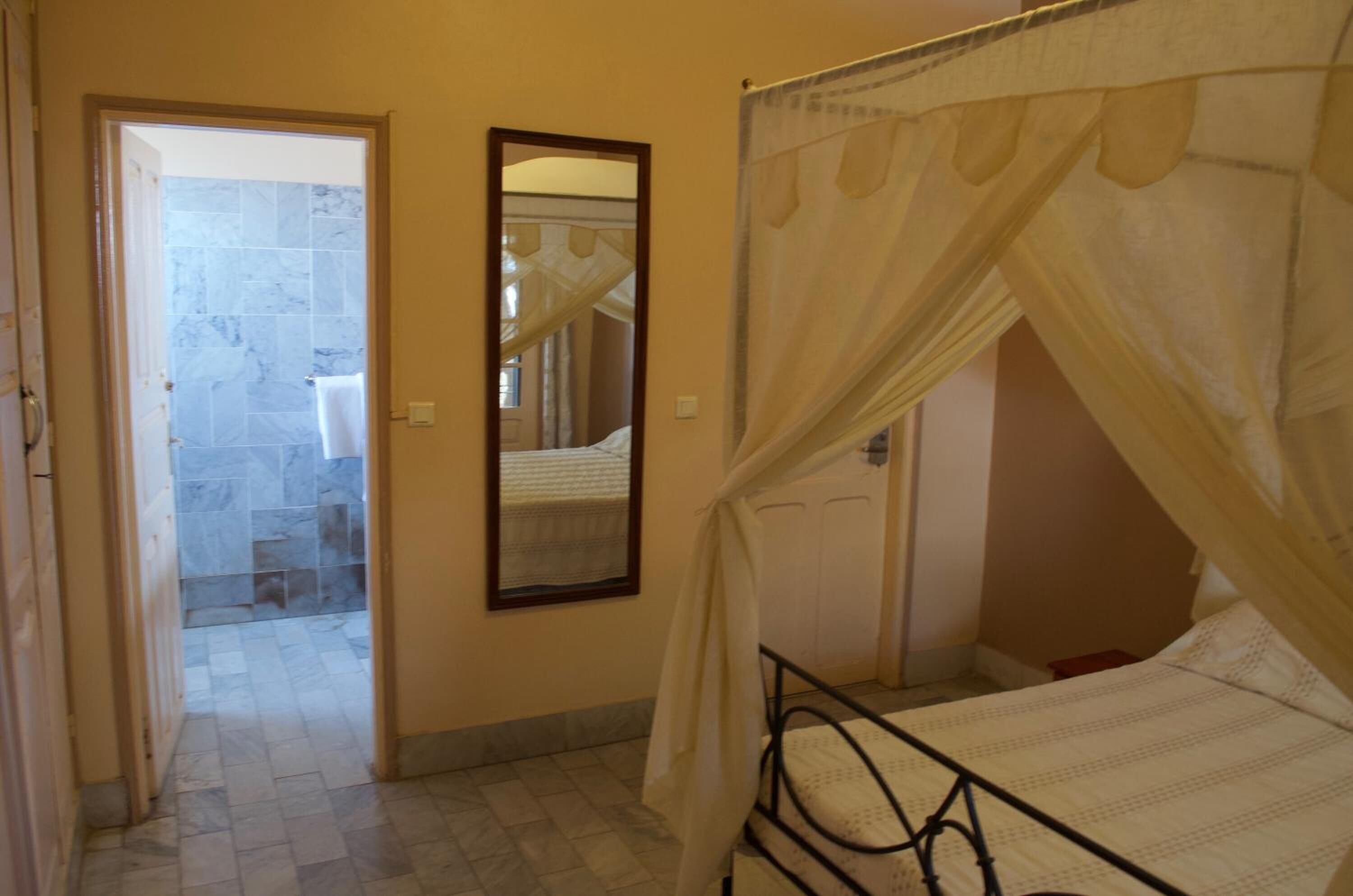 A bedroom with a bed, a mirror, and a door leading to a bathroom with a tiled shower.