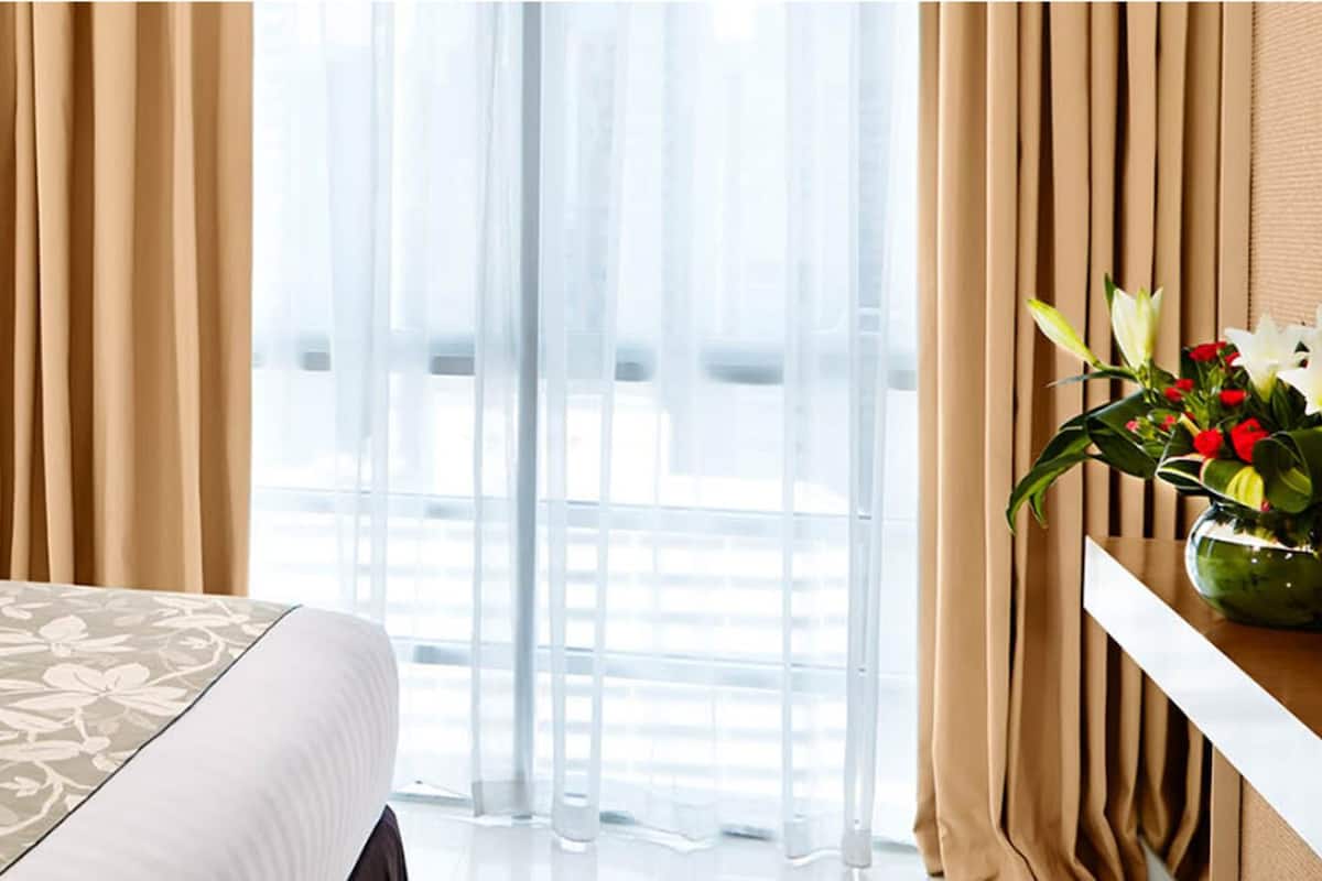 Ein Hotelzimmer mit Bett, cremefarbenen Vorhängen und einem Fenster mit Blick.