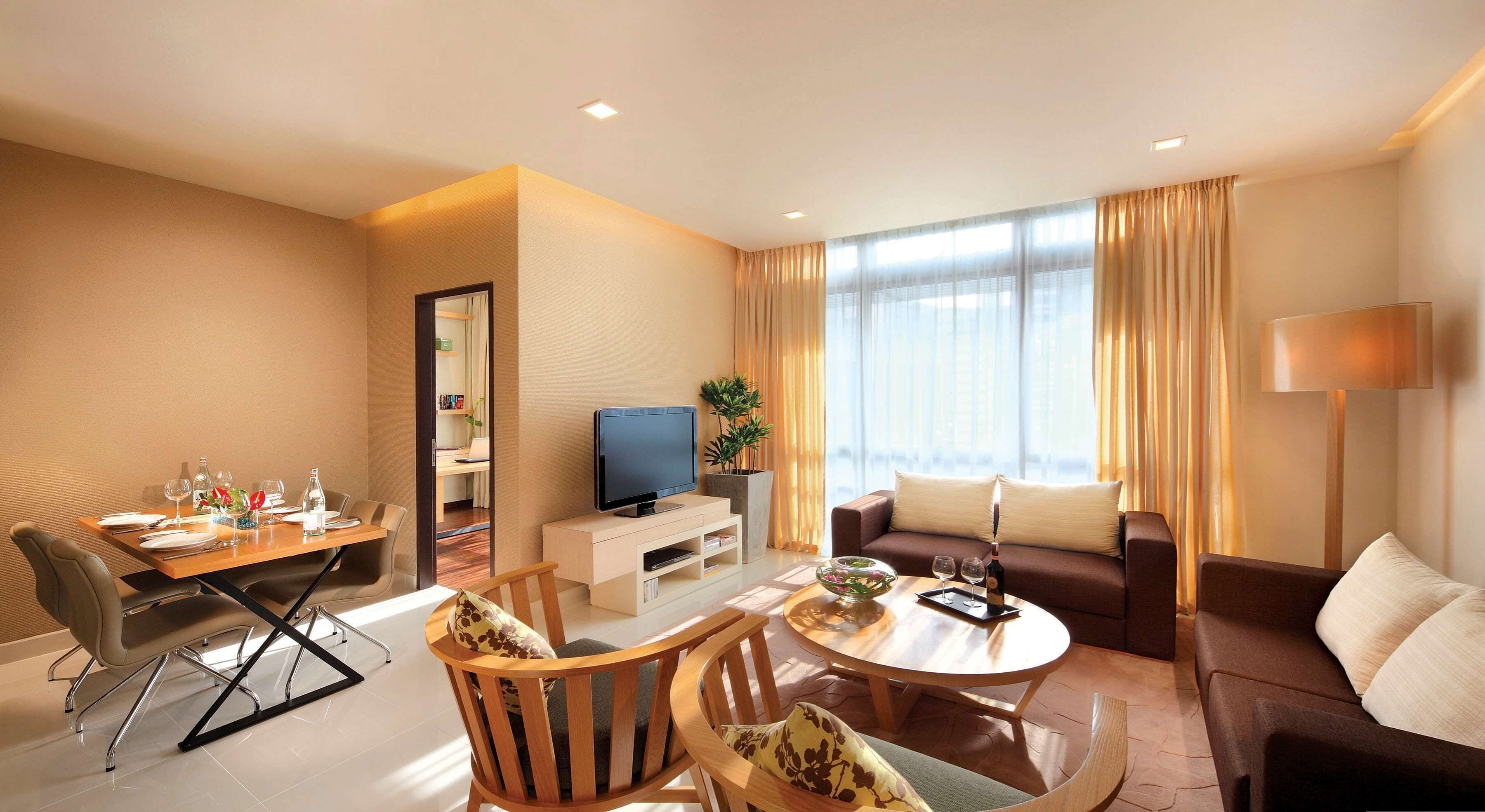 Une chambre d’hôtel moderne comprenant un coin repas, un salon avec un canapé et une table basse, une télévision et une grande fenêtre avec des rideaux.