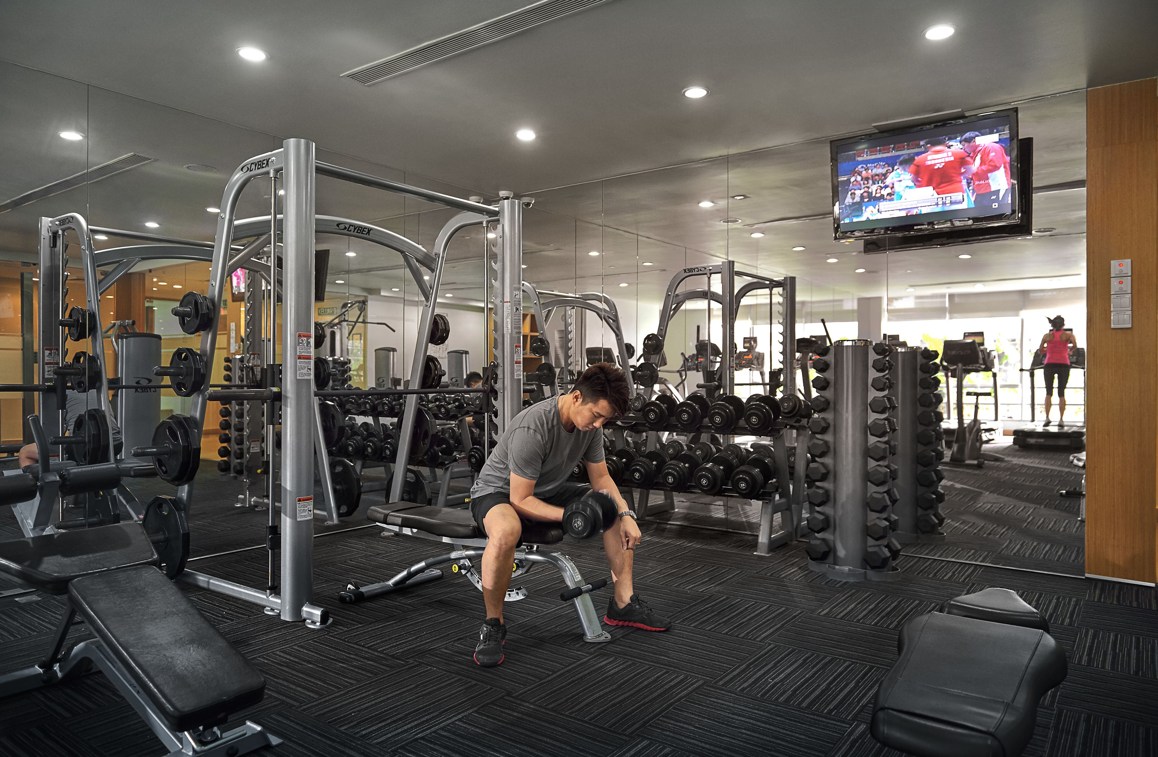 A gym with weightlifting equipment, a television screen, and a person exercising.