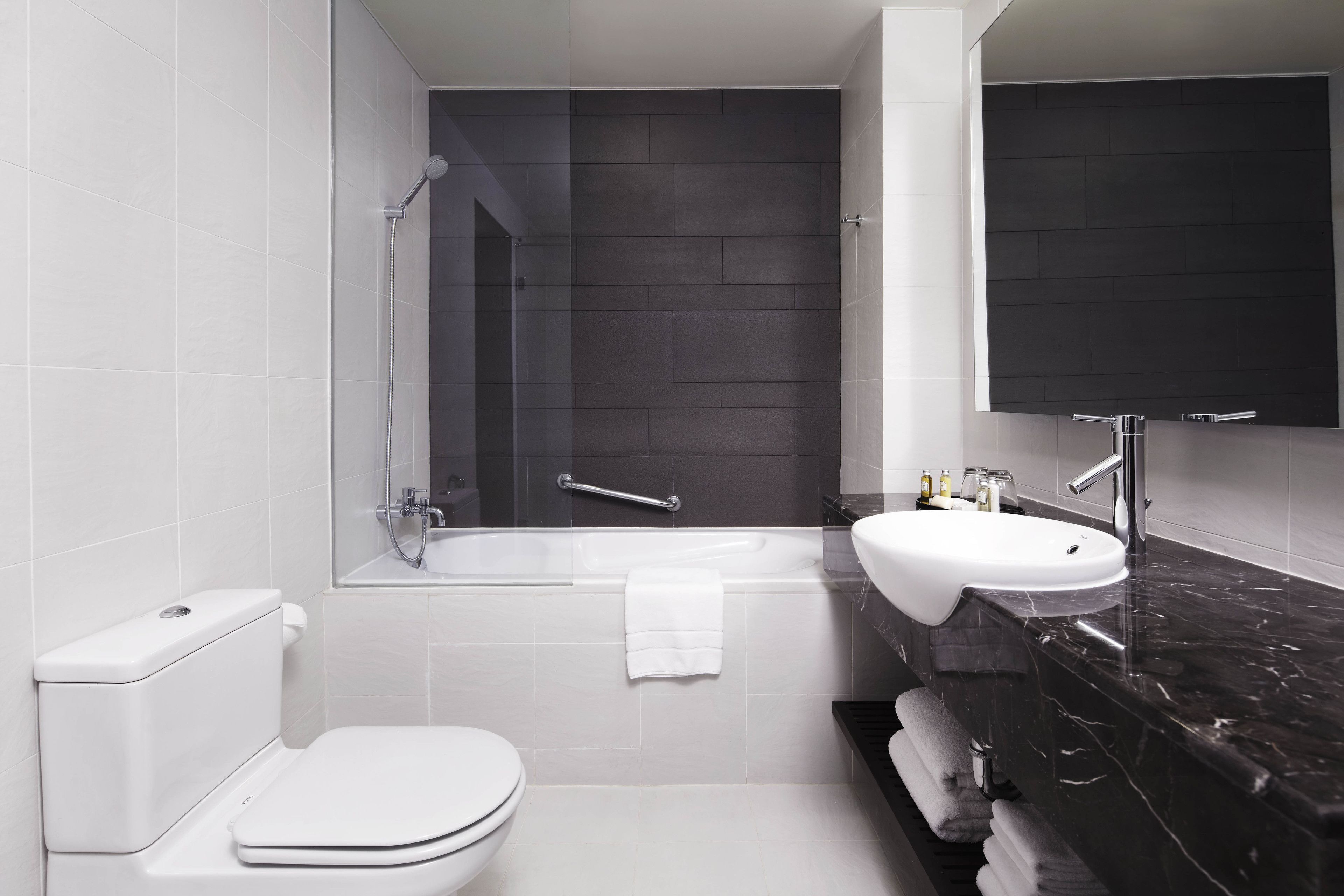 A modern bathroom with a white toilet, a bathtub, and a sink with a dark countertop.
