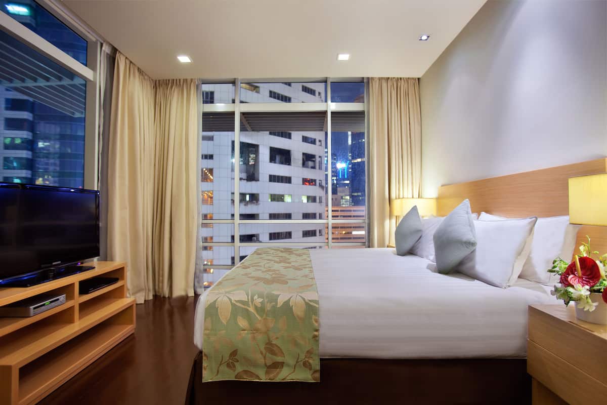 Ein Hotelzimmer mit einem großen Bett, einem Fernseher auf einem Holztisch und einem Fenster mit Vorhängen.