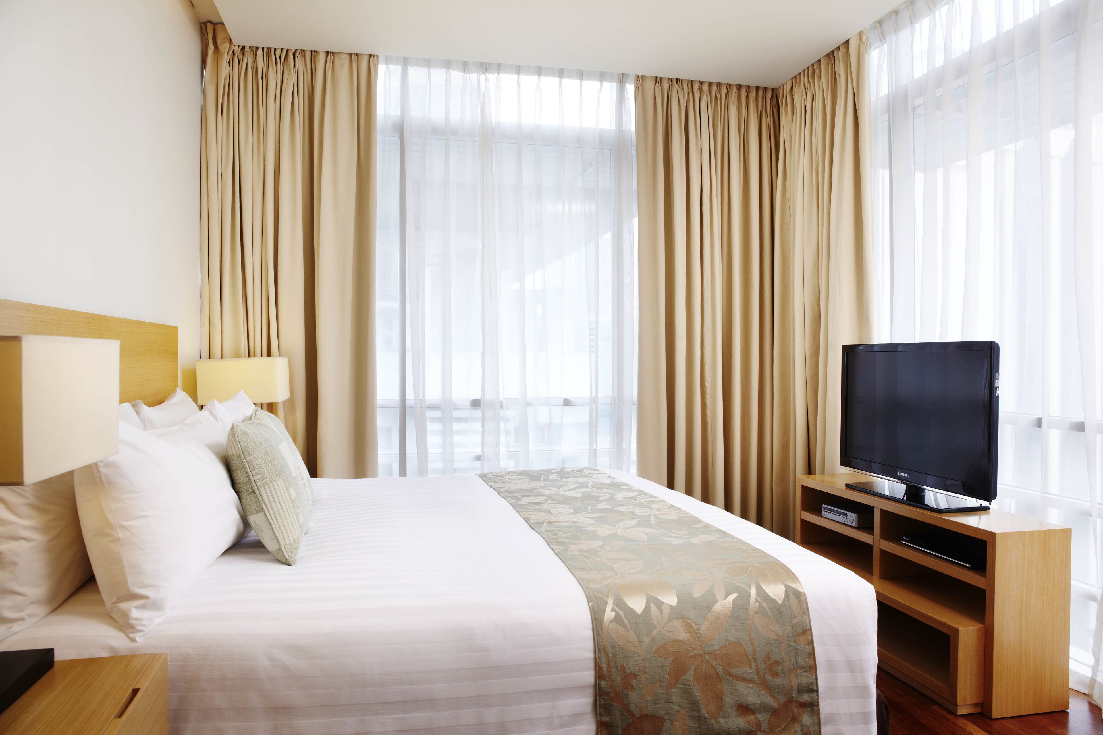 A hotel room with a bed, a TV, a bedside table, and curtains.