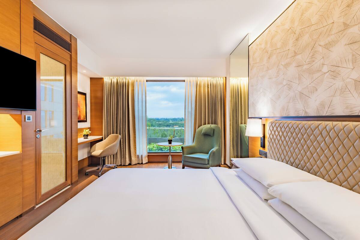 A hotel room with a large bed, a desk, a chair, a TV, and a view of the outdoors.