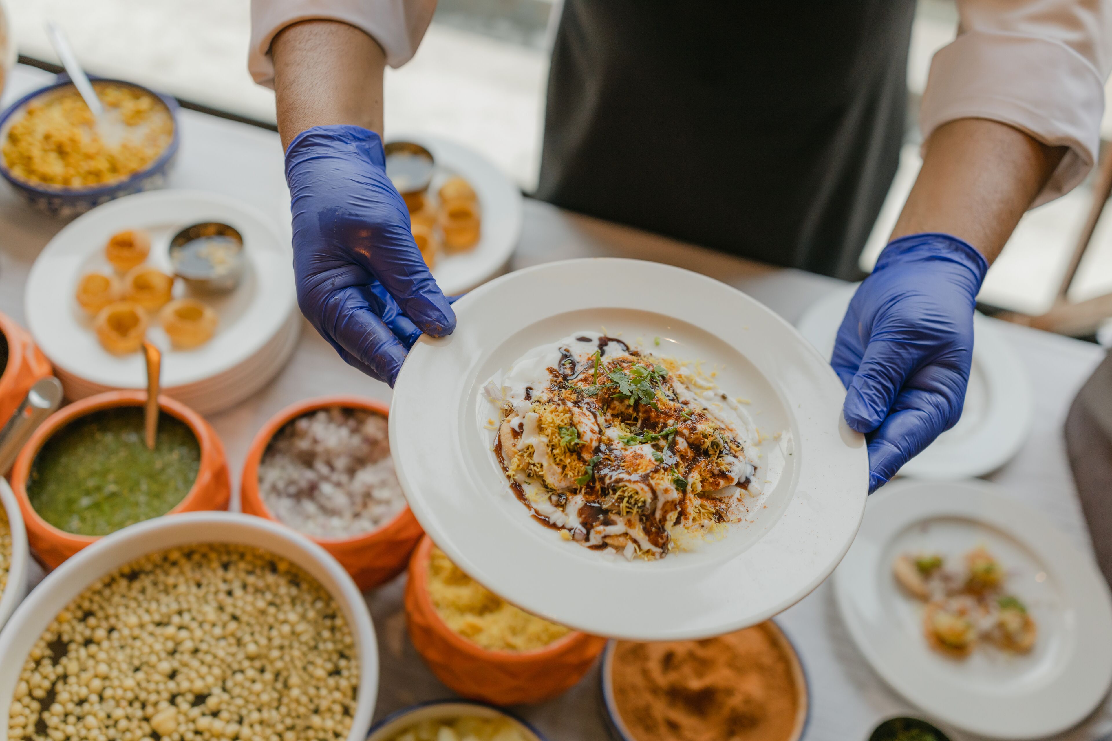 A person wearing gloves serving a dish with various condiments.