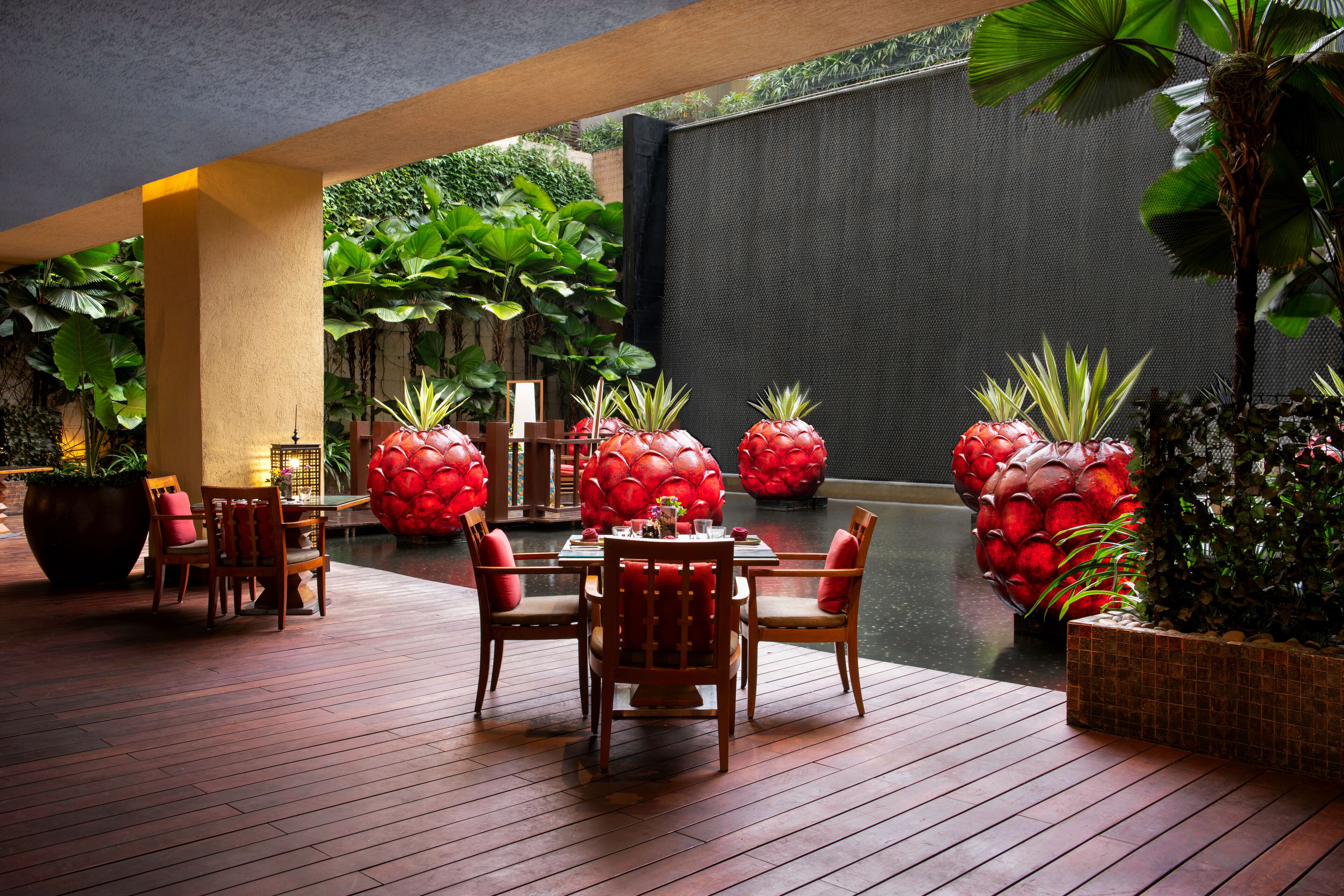 A wooden deck with a table and chairs, surrounded by large potted plants and a water feature.