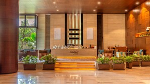 A reception area with a wooden reception desk, potted plants, and a view of greenery outside. - Hyatt Pune (Pune)
