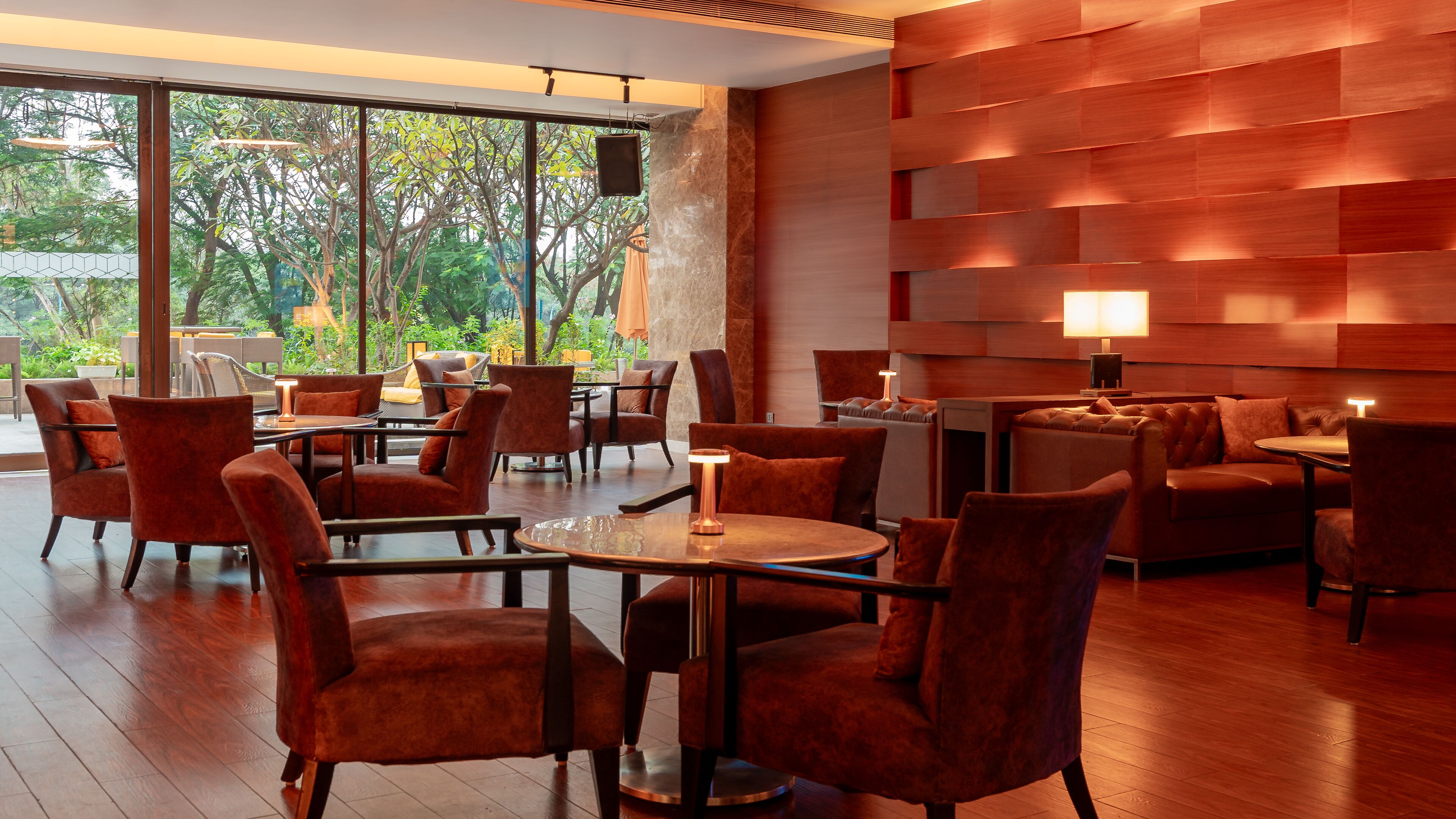 A modern interior with a mix of seating arrangements, including sofas and chairs, arranged around tables. Large windows provide a view of the outdoors.