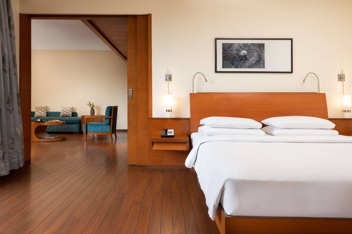 A hotel room with a wooden bed, a bedside table with a phone, a wall-mounted picture, and a seating area with a sofa and armchairs.