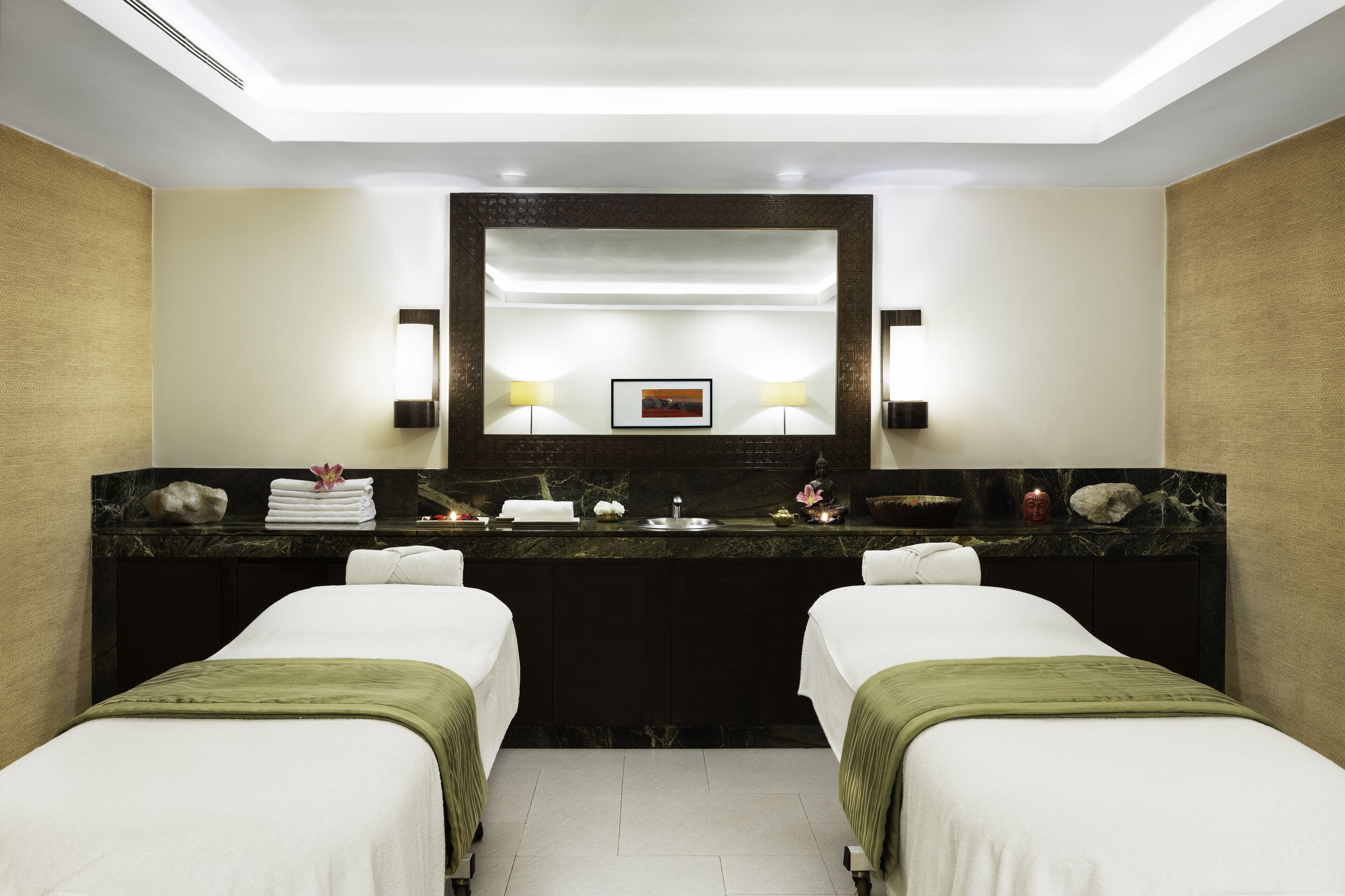 A hotel room with a large mirror, two beds, a marble vanity with a sink, and a framed picture above the mirror.