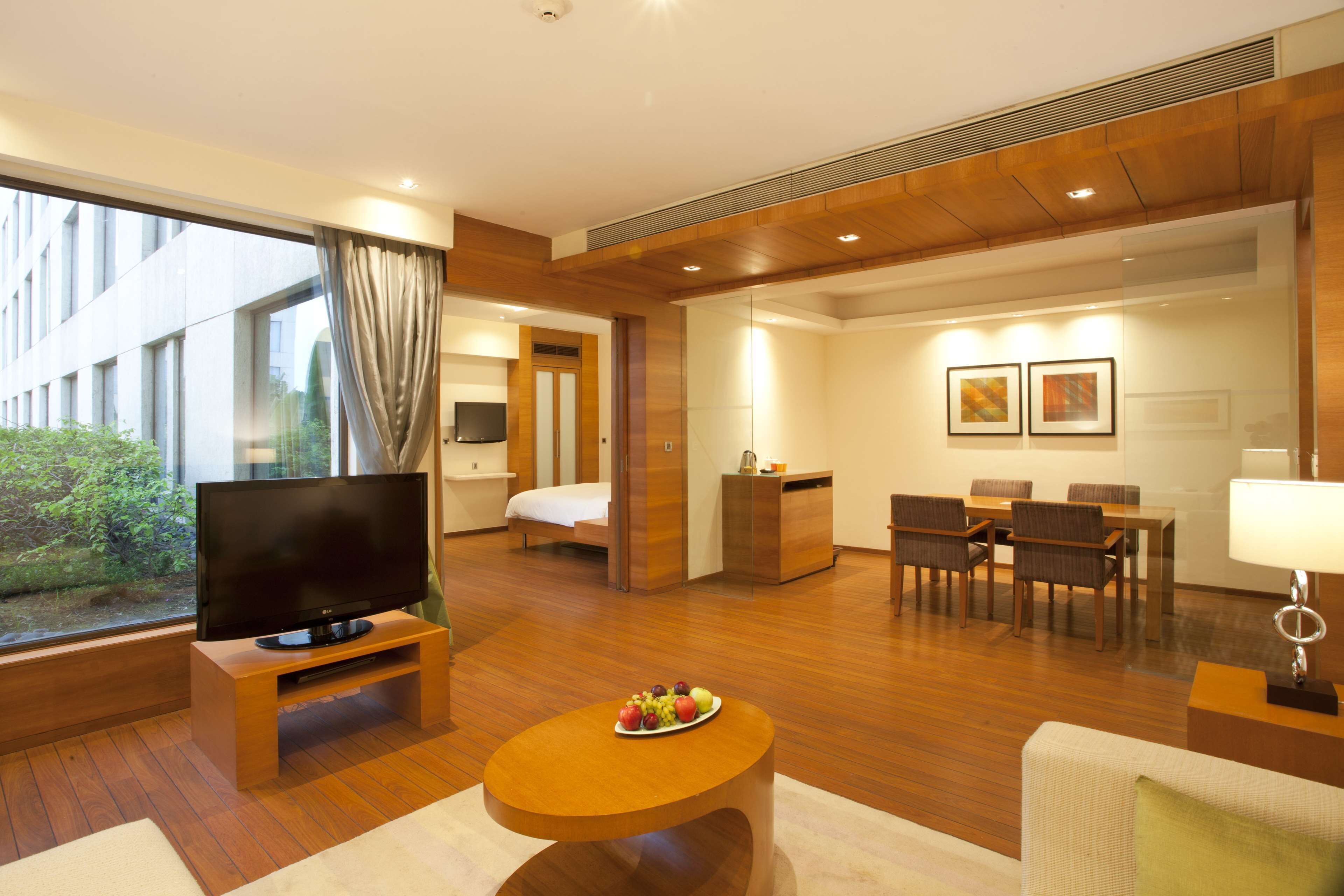 A modern hotel room with a TV, dining area, and a large window.
