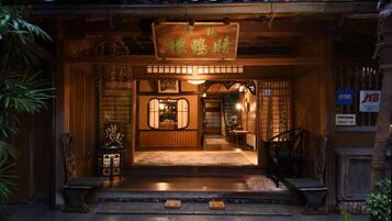 A traditional Japanese entrance with a wooden sign, a tiled roof, and a stone pathway leading to the entrance.