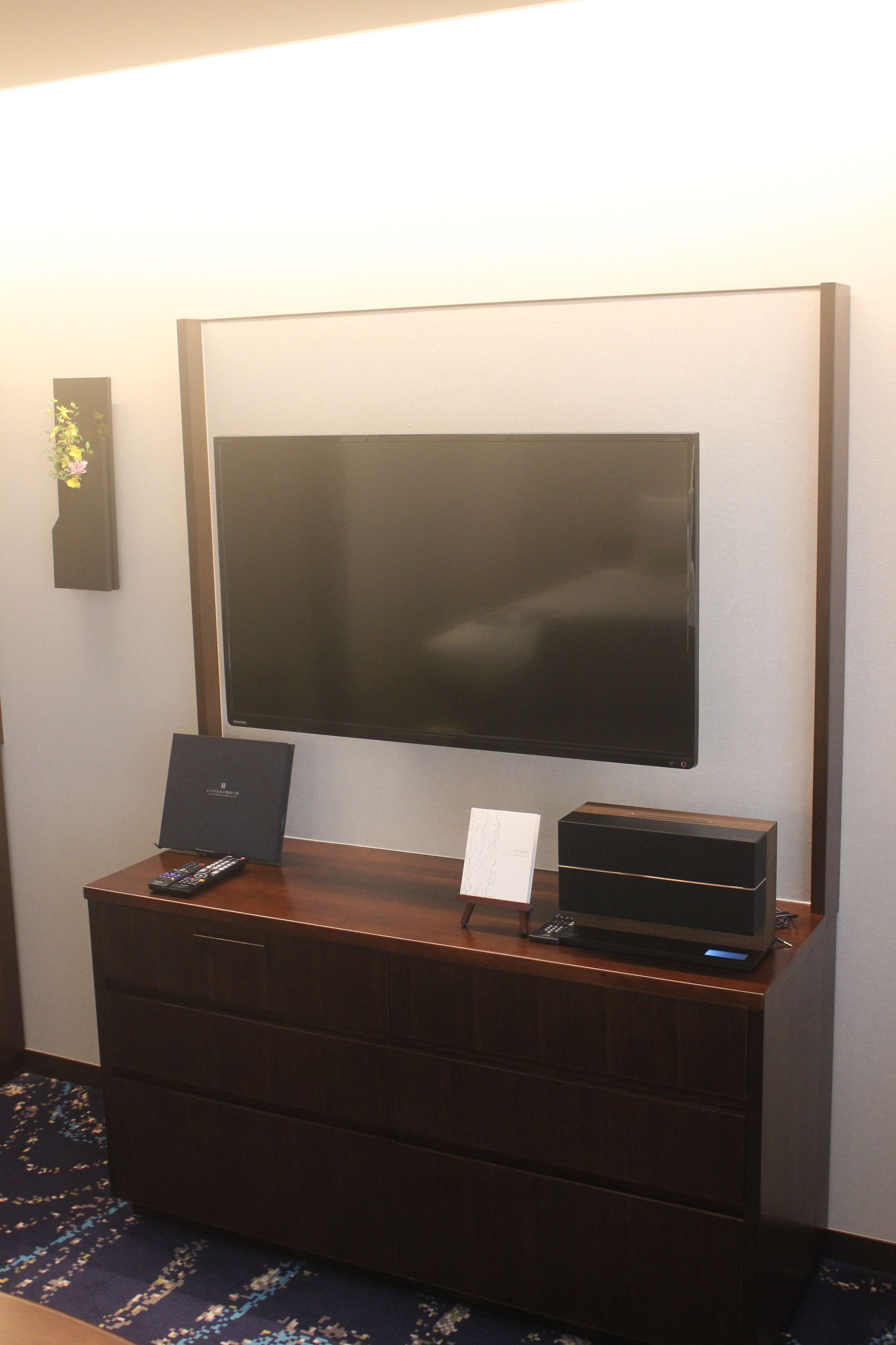 A flat-screen TV mounted on a wall above a wooden dresser.